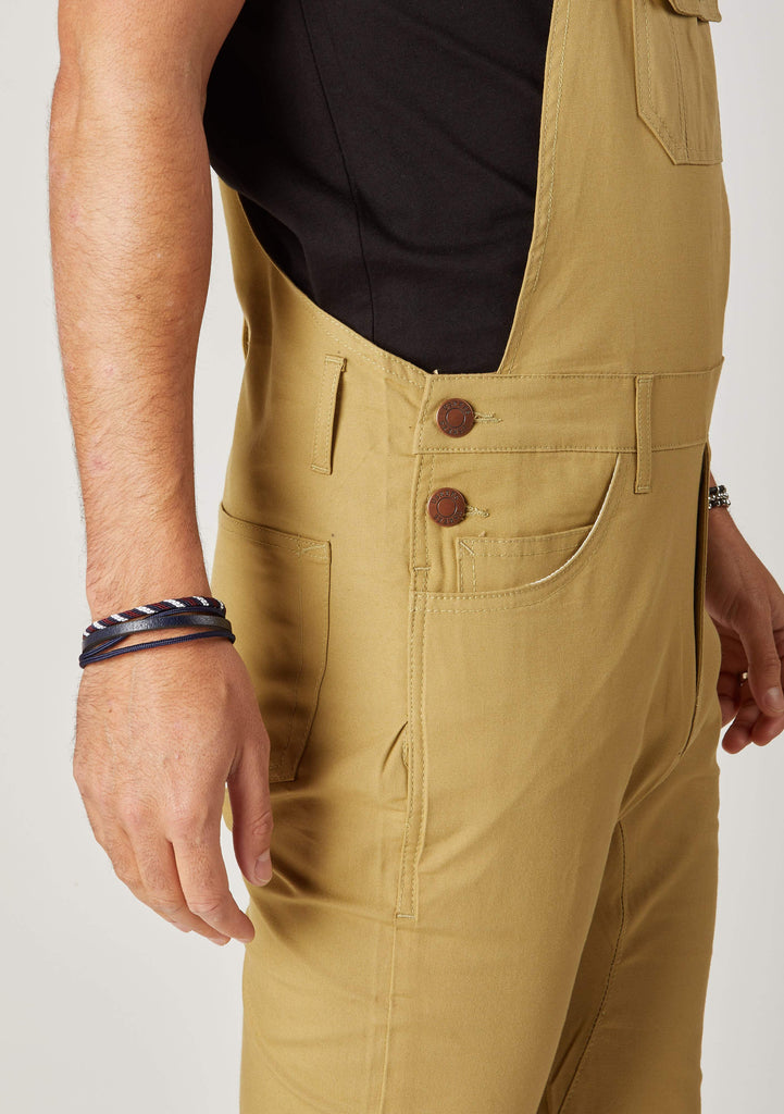 Close-up side view of men’s slim-fit black khaki bib-overalls with clear view of side button fastening and belt loops.