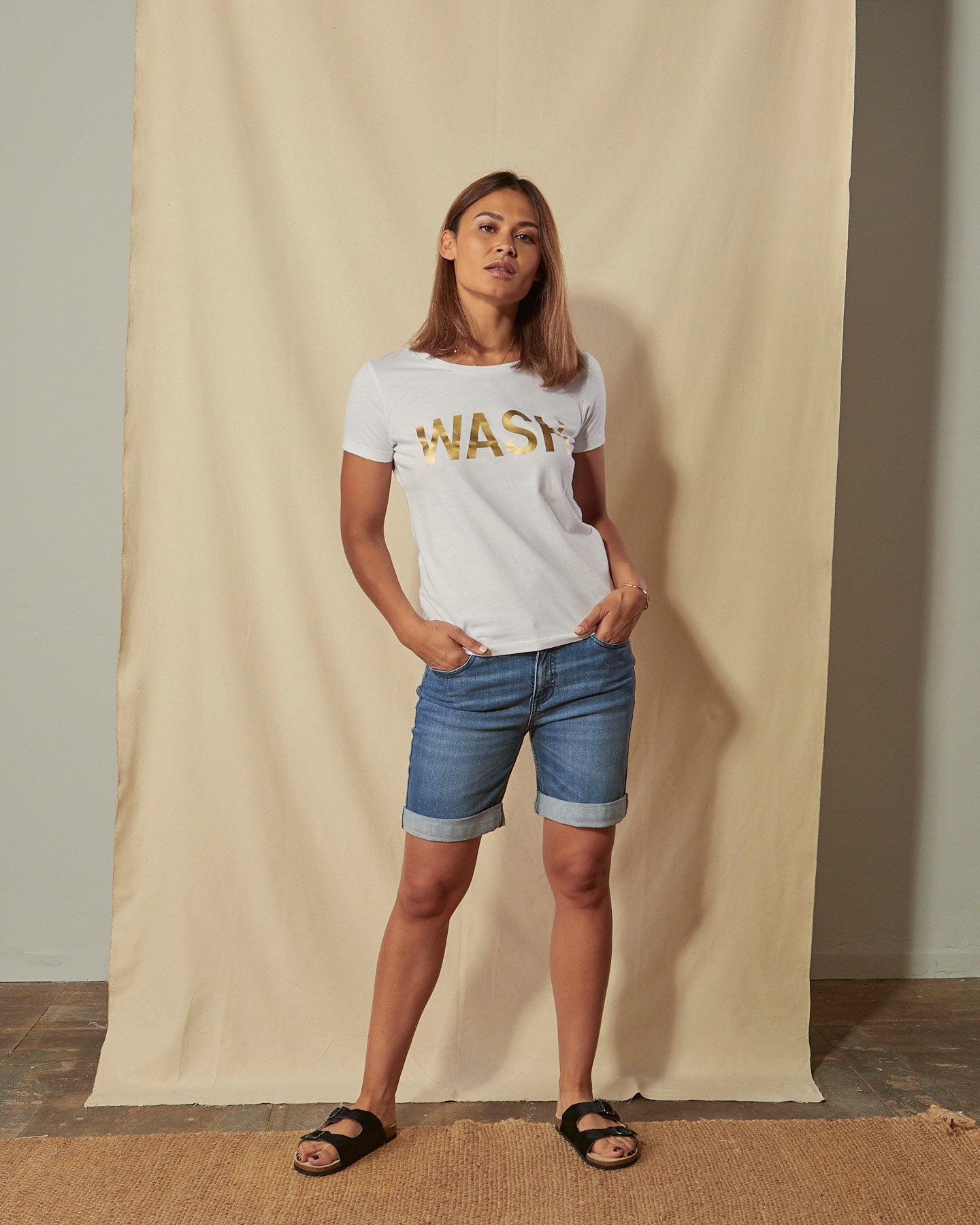 Full-length front view of model with hands in pockets of Enya organic denim shorts.
