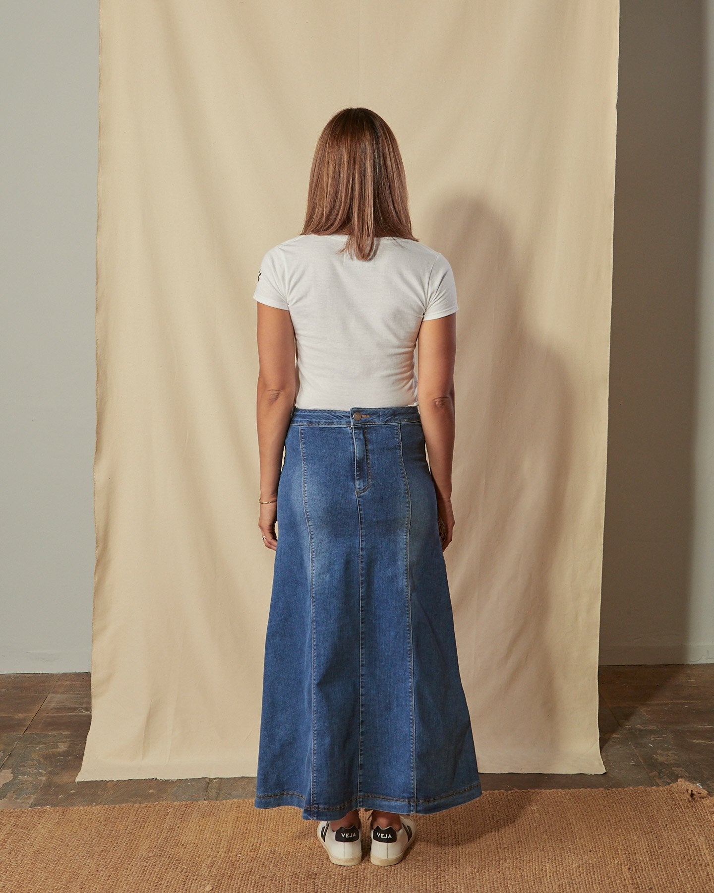 Full-length back view of model wearing A-line panelled denim skirt showing figure-hugging stretch denim and ankle length hem with no back split.