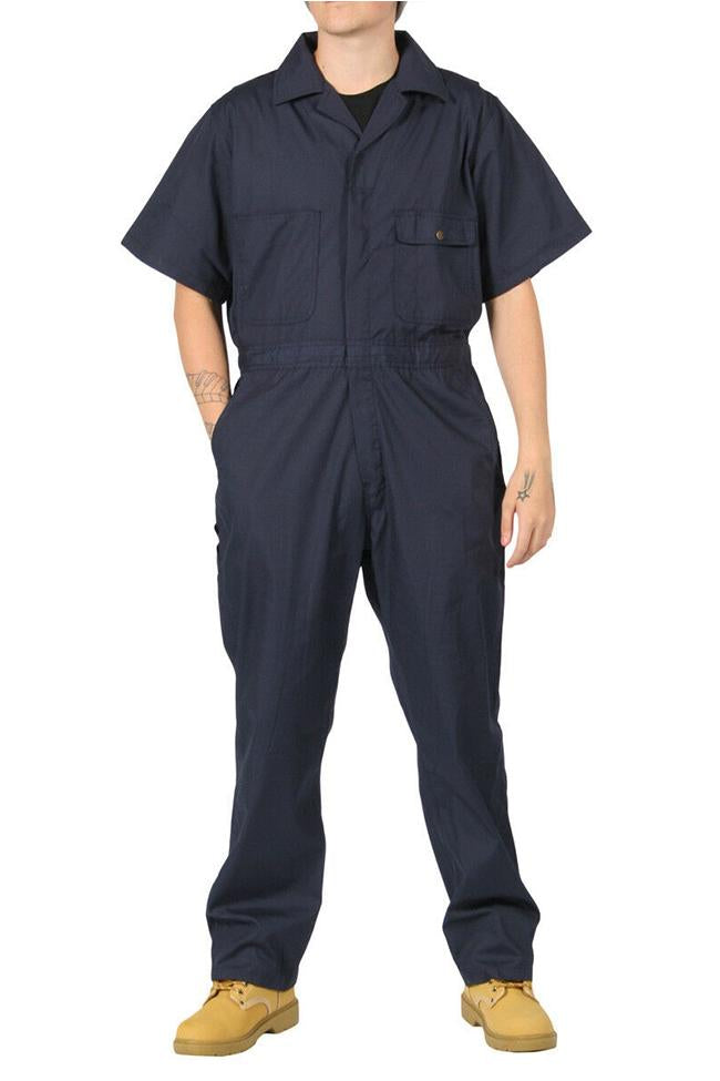 Full-length front view with hands in right pocket, wearing ‘Key Apparel USA’ relaxed-fit navy coverall, showing chest pockets.