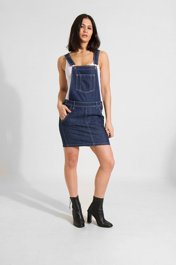 Slightly distant, full frontal pose looking straight ahead with right hand in pocket, wearing indigo denim dungaree dress from Dungarees Online.