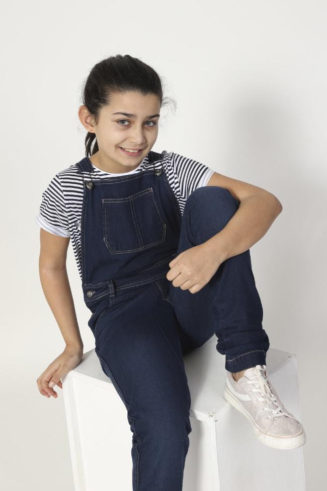 Girl sitting on box, wearing durable machine washable, Libby style kids overalls from Dungarees Online.