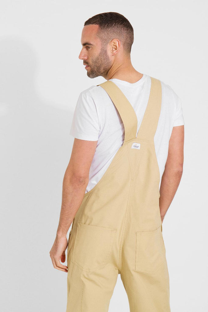 Looking to his left with back to camera focussing on top half of ‘Christopher’ brand dungaree shorts.