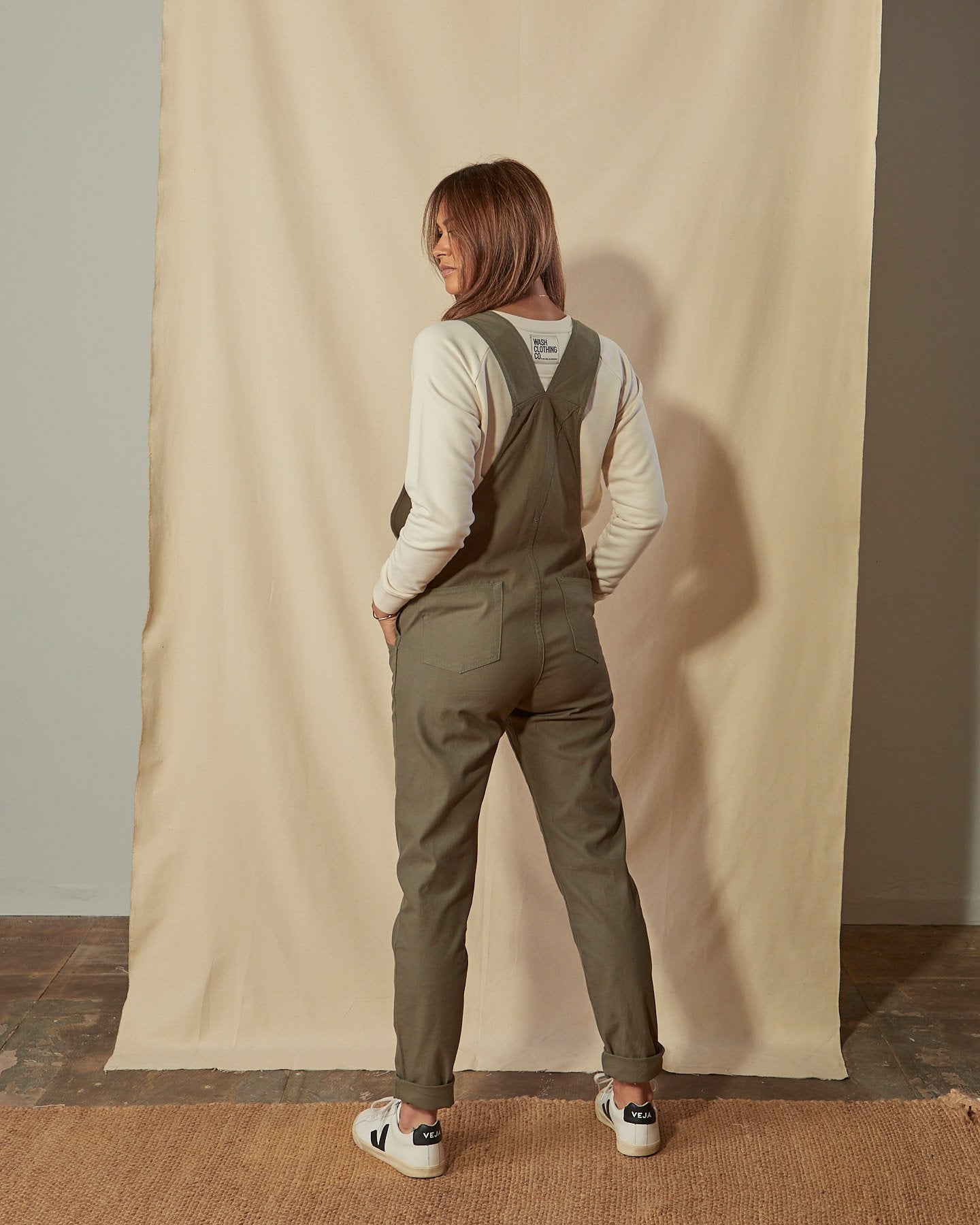 Full-length back view of model wearing Harper green organic cotton dungarees showing back pockets and straps.