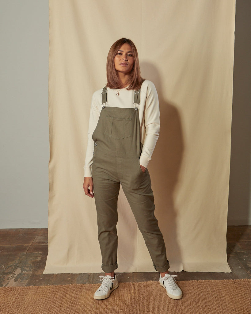 Full-length front view of model wearing Harper green organic cotton dungarees with hand in front pocket.