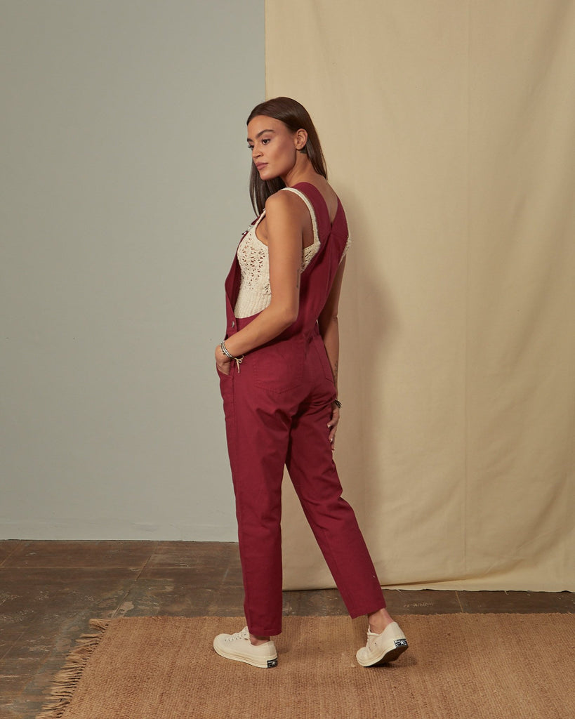 Full-length side view of model wearing Harper red organic cotton dungarees showing back pockets and straps.