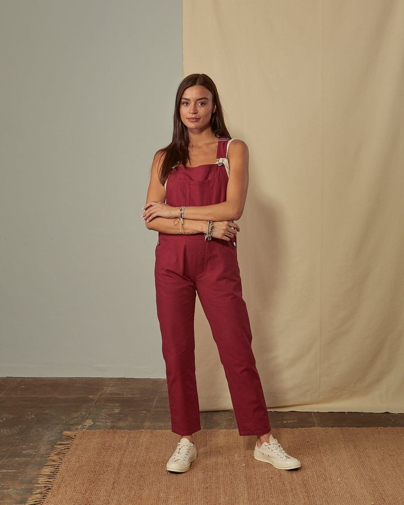 Full-length front view of model wearing Harper red organic cotton dungarees showing tapered leg.