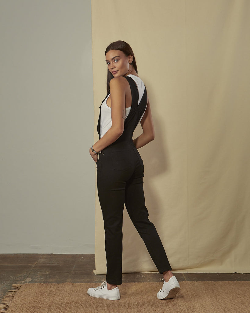 Full-length side view of model wearing Kate black cotton dungarees demonstrating narrow, figure-hugging fit.