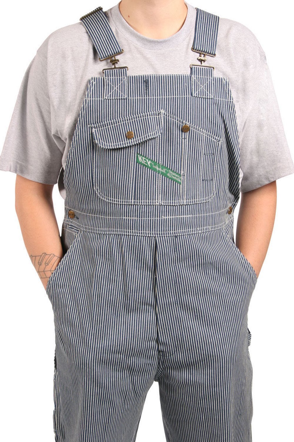 Close-up mid-section frontal of striped work bib-overall, showing multiple bib pockets, robust seams, zip fly and adjustable straps, with hands in front pockets.
