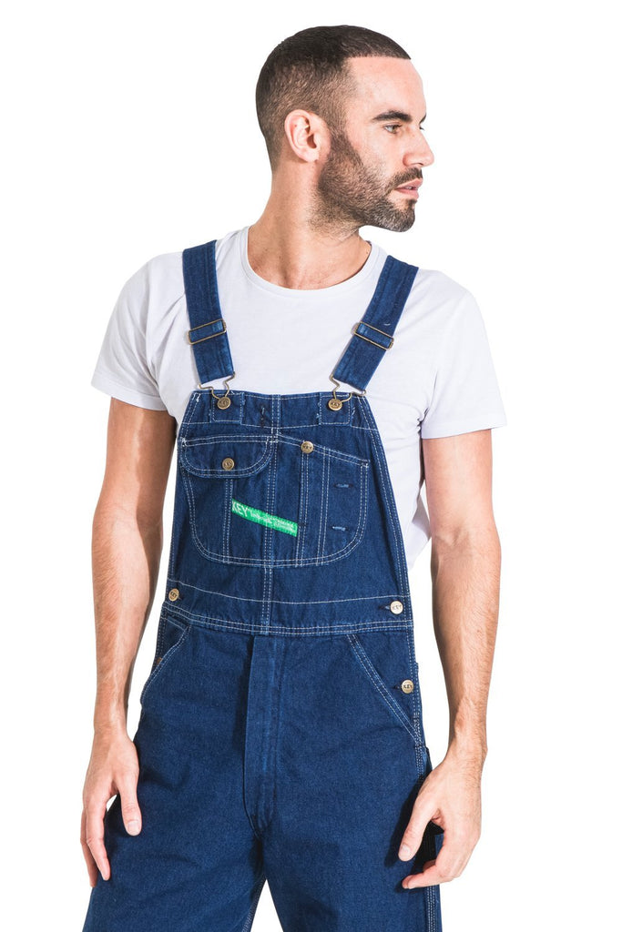 Top-half front view of indigo work bib-overall, showing multiple pockets, robust seams, zip fly and adjustable straps.