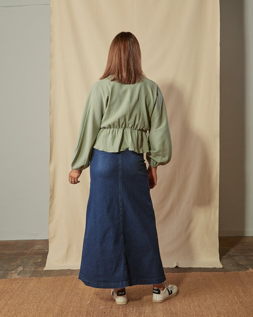 Full-length front view of model with hands in front pockets and view of belt loops of Kingsley flared long denim skirt.