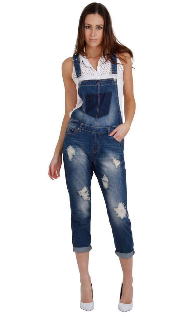 Full-length front view of women's denim dungarees with wiew of adjustable straps and extensive rips, abrasion and fraying detail.