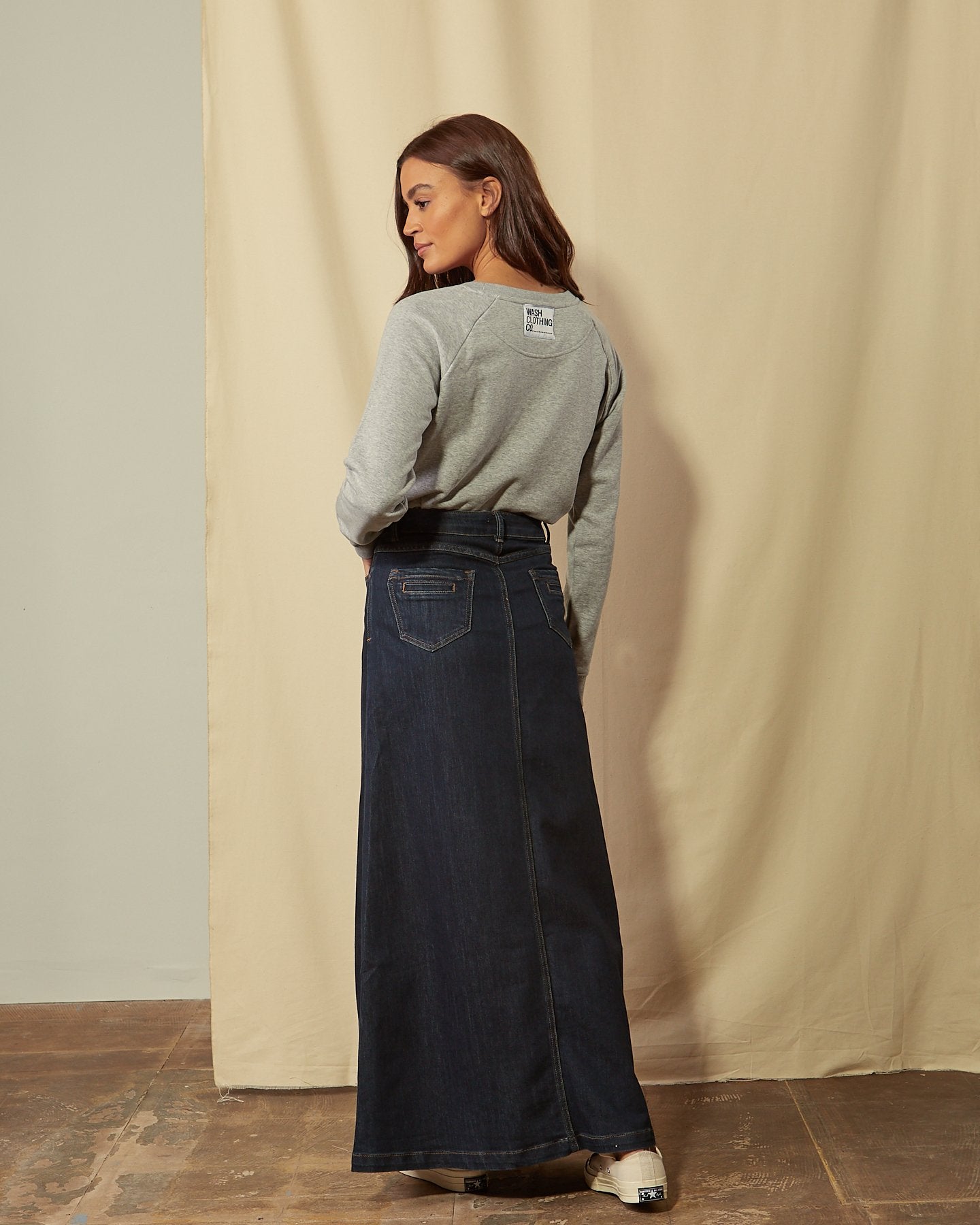 Full-length back view of dark blue flared style skirt accentuating stretch properties of denim with view of back pockets.