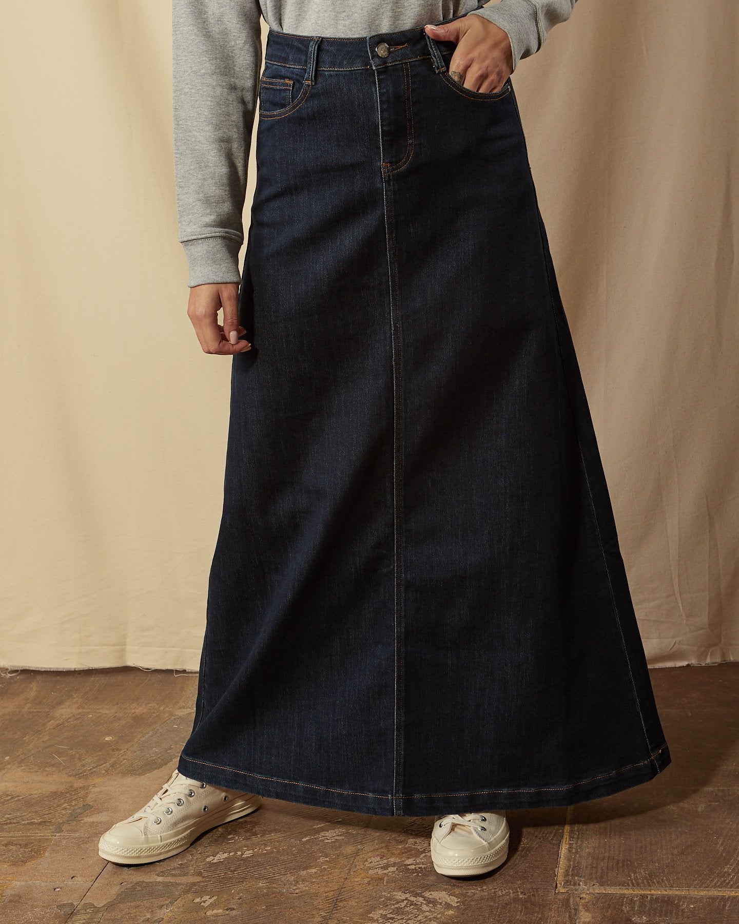Close-up front view of dark blue flared style denim skirt with focus on front pockets, belt loops and button closure.