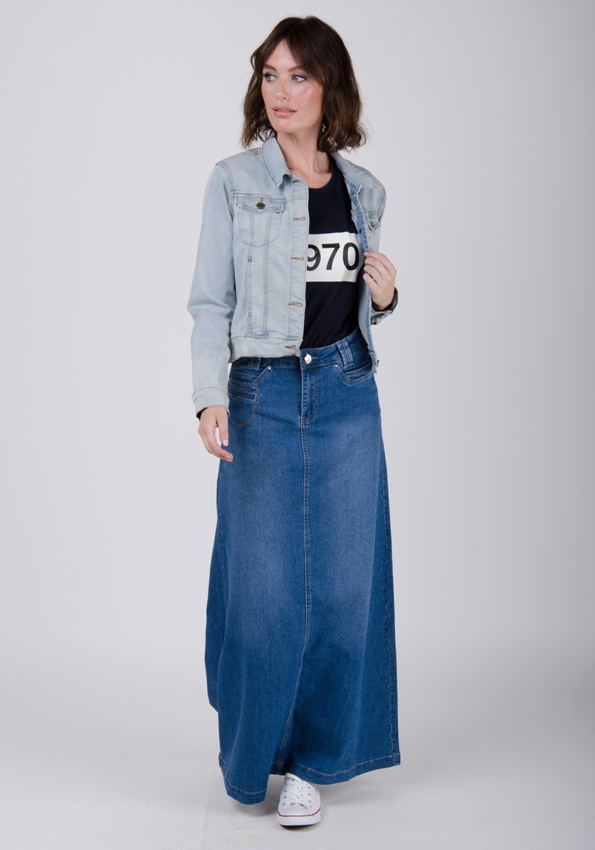 Full-length front walking pose of stonewash flared style denim skirt with view of belt loops and button closure and paired with light denim jacket.
