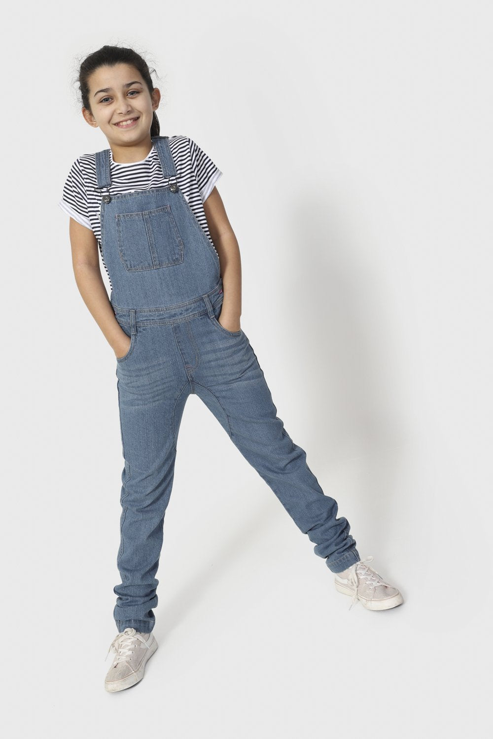 Full-length front pose with legs apart and hands in front pockets wearing Libby-style palewash dungarees with large bib pocket.