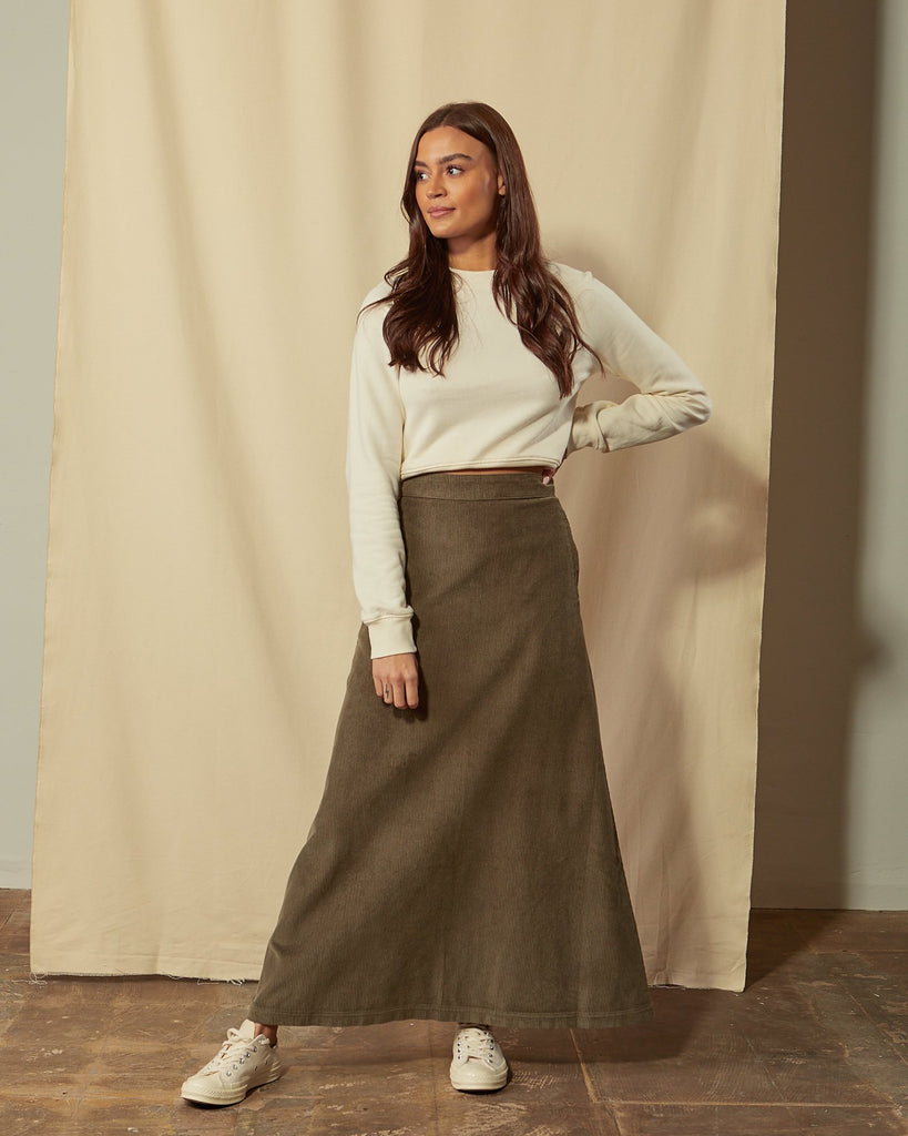 Full-length front view of model wearing Lottie olive-green corduroy maxi-skirt with hand on hip.