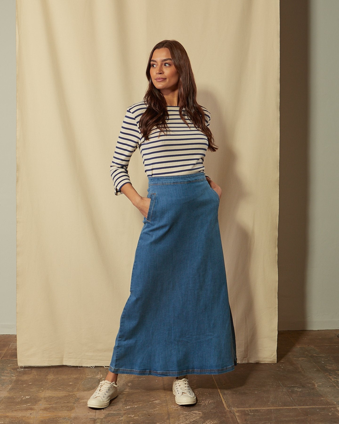 Full-length front view of model with hands in pockets of Lottie palewash denim maxi-skirt.