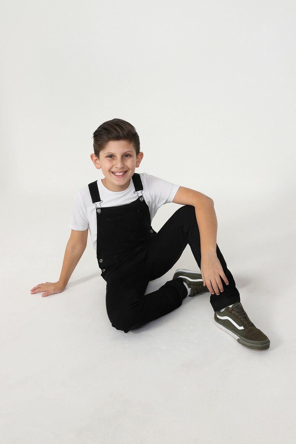 Boy sitting on floor wearing ‘Matthew’ style dark overalls.