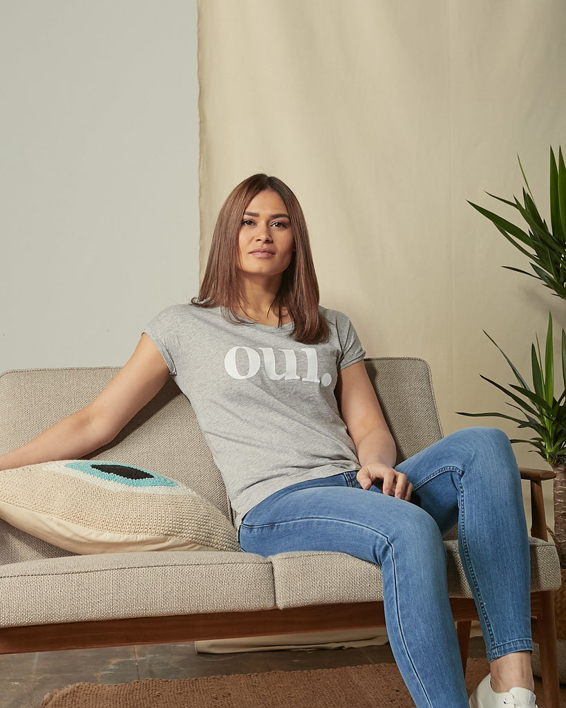 Lounging on sofa wearing 'Oui' motif cotton t-shirt in grey.