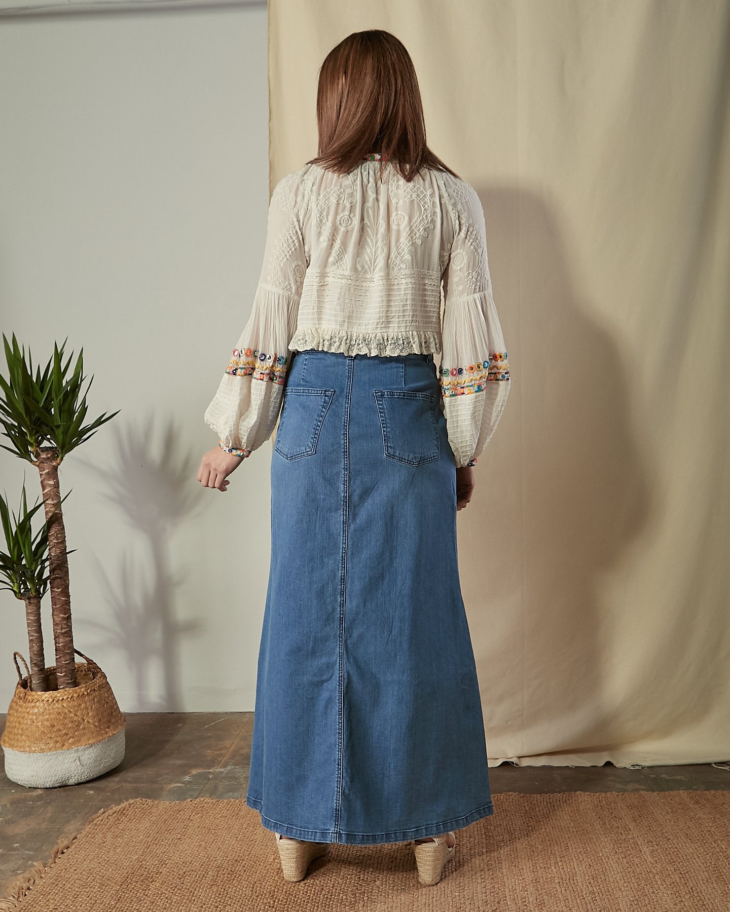 Full-length back view of organic cotton maxi denim skirt with view of back pockets, center seam and subtle flaring.
