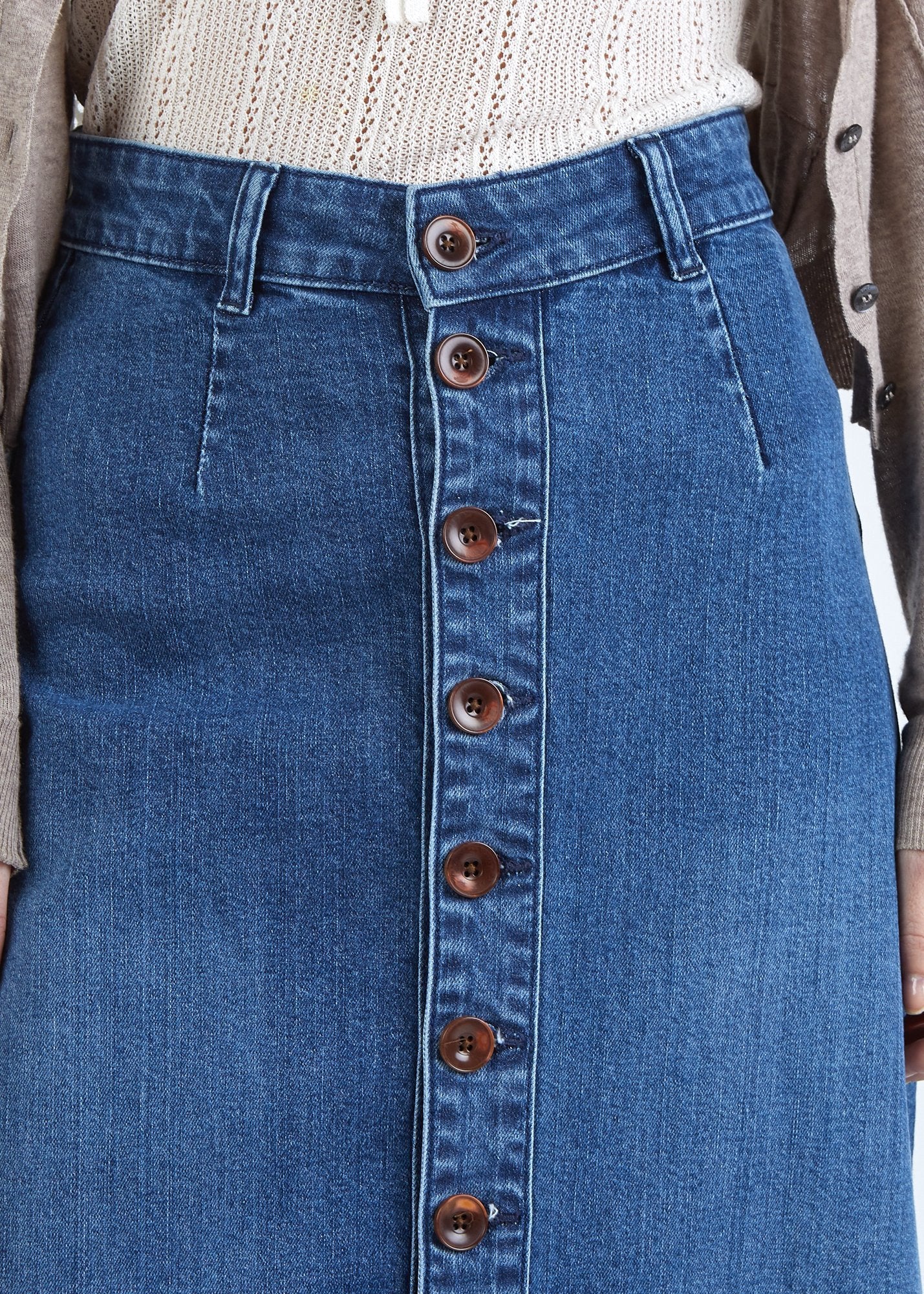 Close-up, midriff view of ‘Peggy’ blue denim skirt with focus on belt loops, button front and organic blue cotton denim.