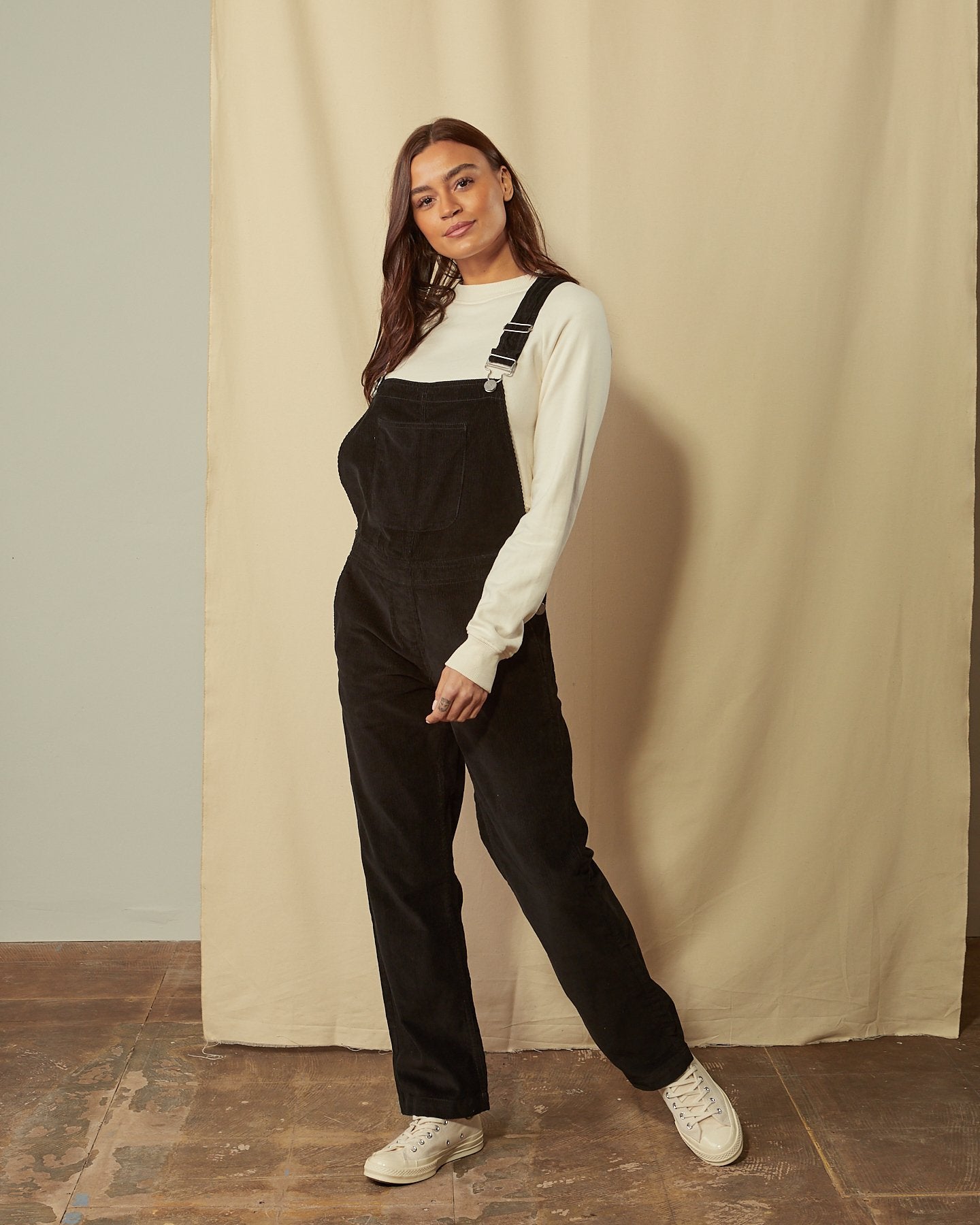 Full-length front view of model wearing Prue black corduroy dungarees with view of large bib pocket.