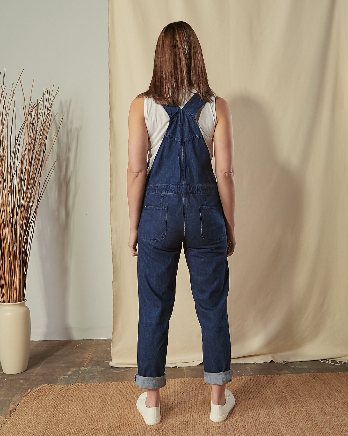 Full-length back view of model wearing Prue blue cotton dungarees with view of back pockets and straps.