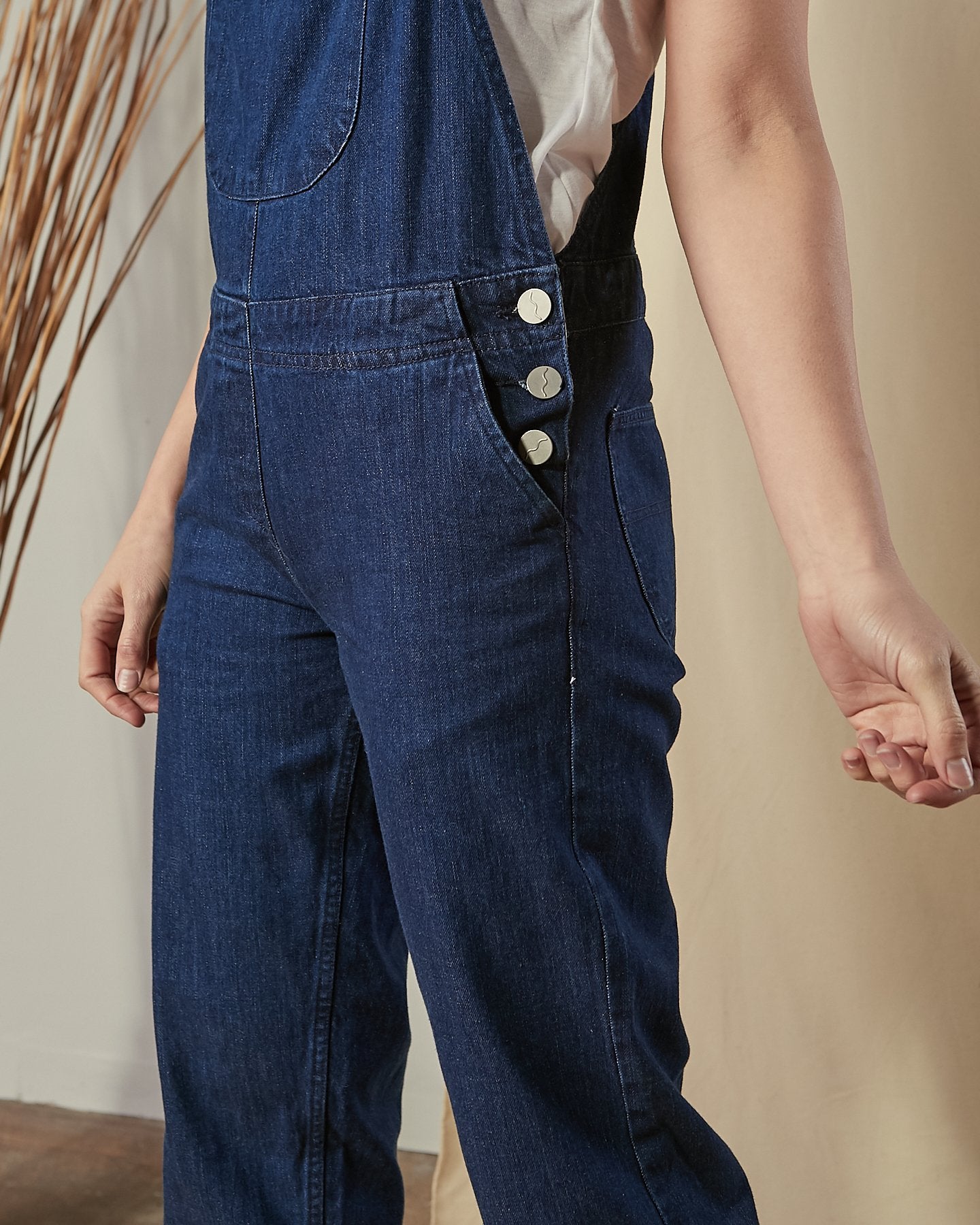 Bottom-half view of model wearing Prue blue cotton dungarees with view of 3-button side fastening and front pockets.