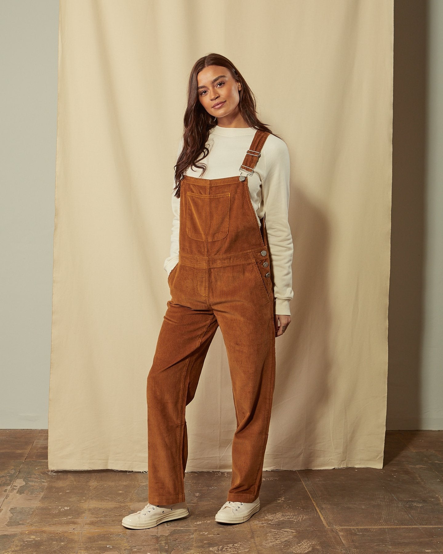 Full-length front view of model wearing Prue brown corduroy dungarees with view of large bib pocket.