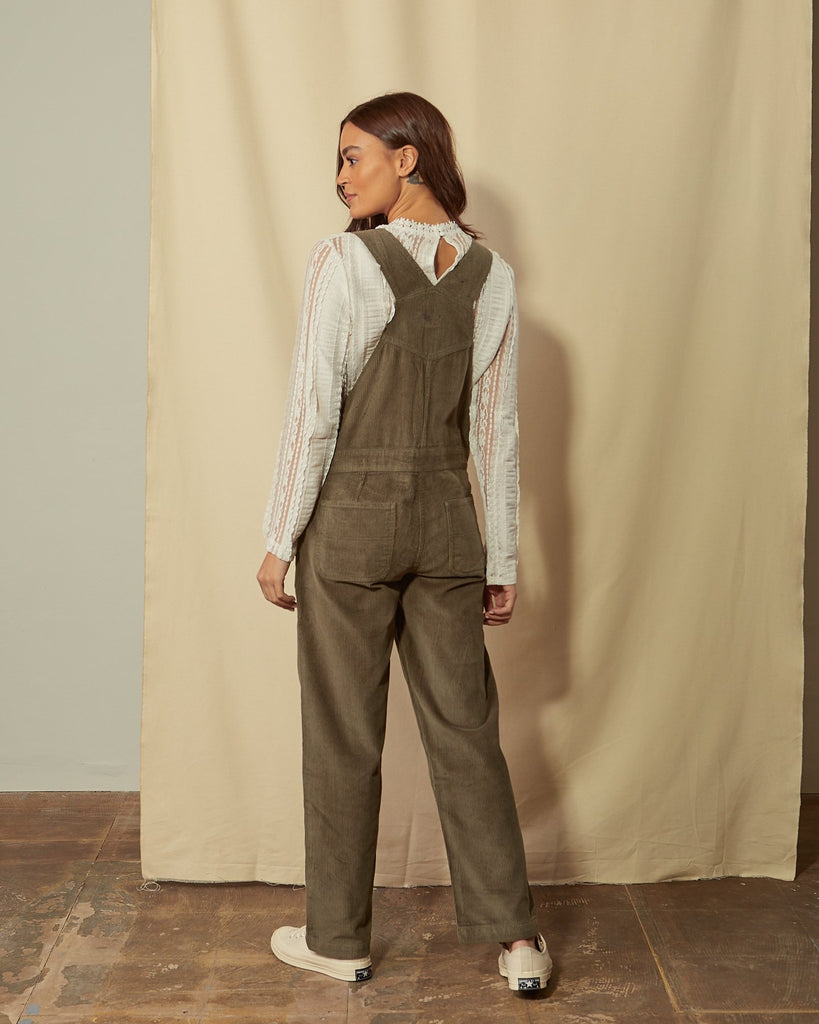 Slightly angled front view of the top-half of model wearing Prue olive corduroy dungarees with view of 3-button side fastening and adjustable buckle straps.