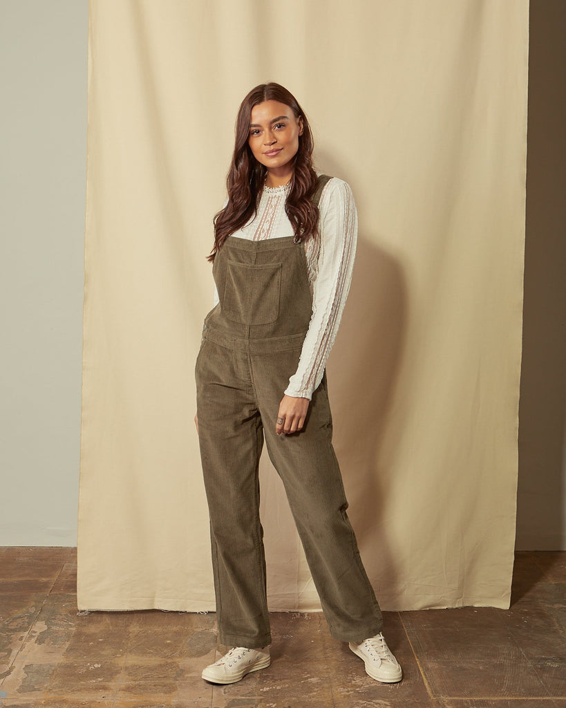 Full-length front view of model wearing Prue olive-green corduroy dungarees with view of large bib pocket.