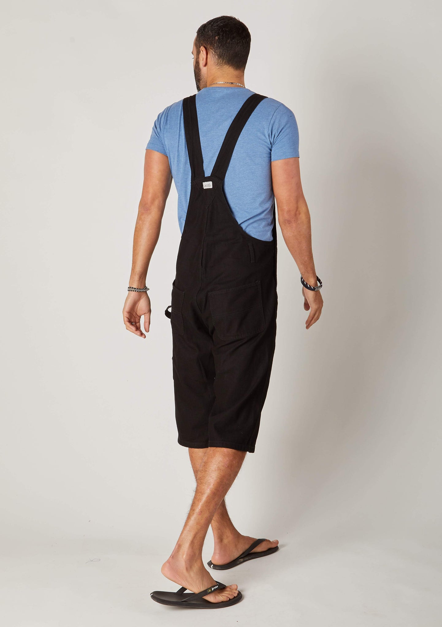 Rear twisted pose wearing ‘Chet’ brand black bib overalls shorts from Dungarees Online.