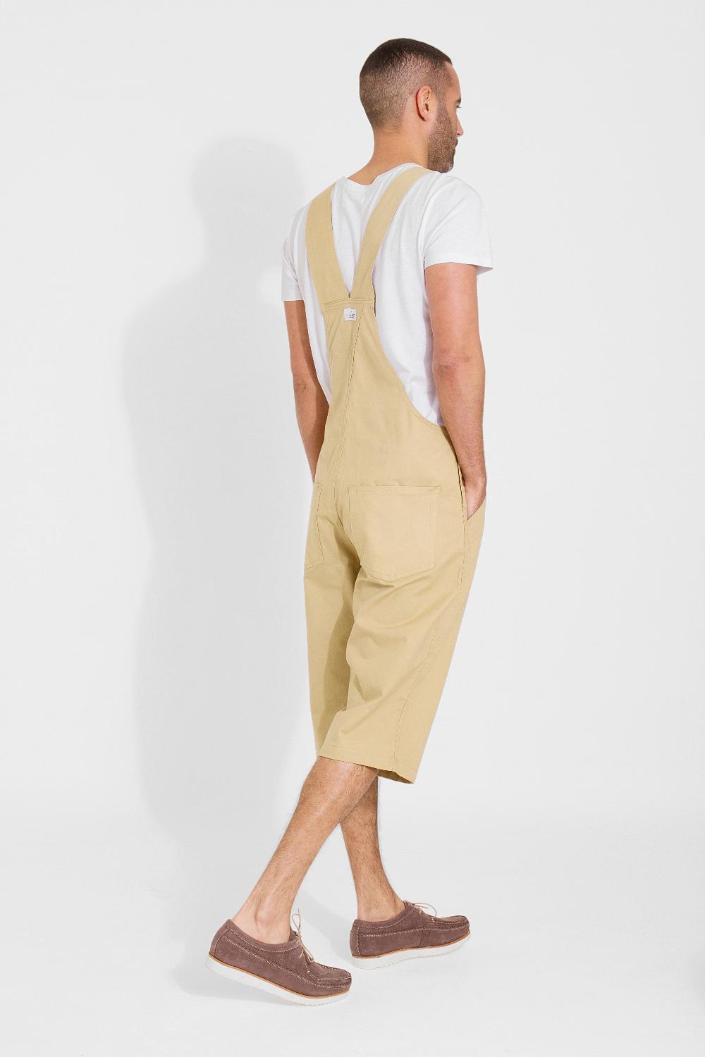 Full rear pose angled to his right, walking with hands in side pockets wearing contemporary dungaree shorts.