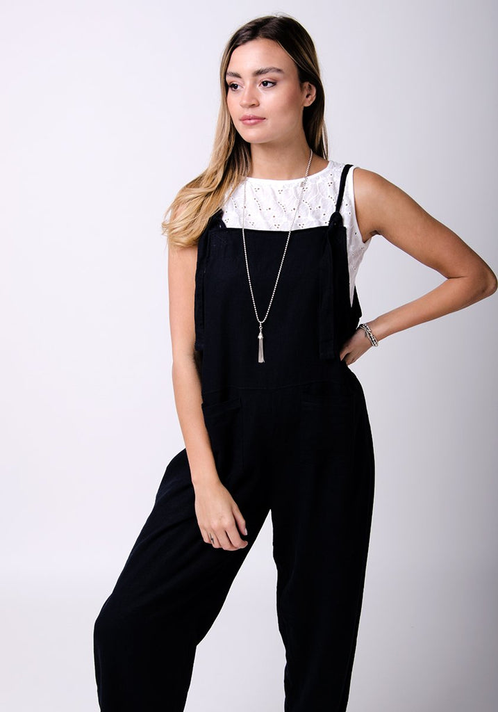 Two-thirds pose with left hand on hip, wearing basic linen, dungaree style jumpsuit.