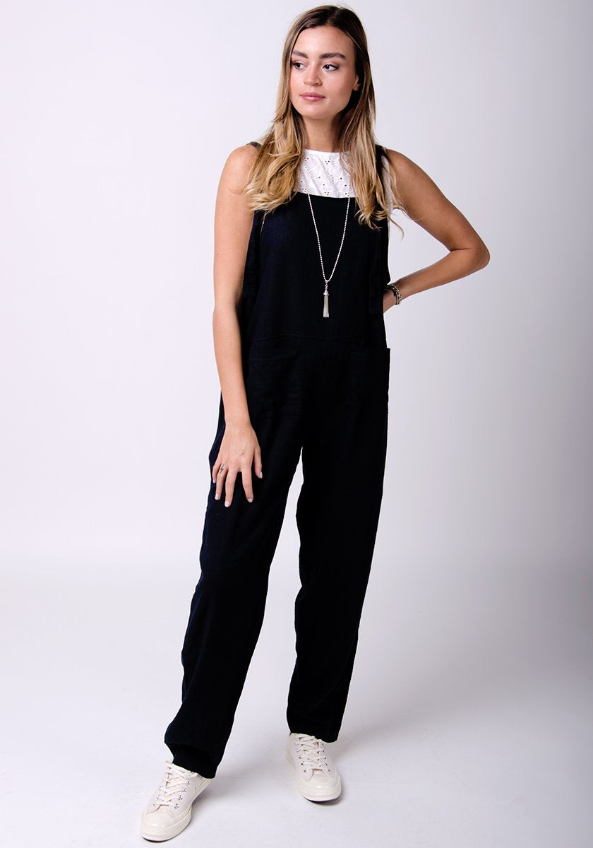 Full-frontal pose with left hand on hip, wearing practical, Roxanne-style linen dungarees.