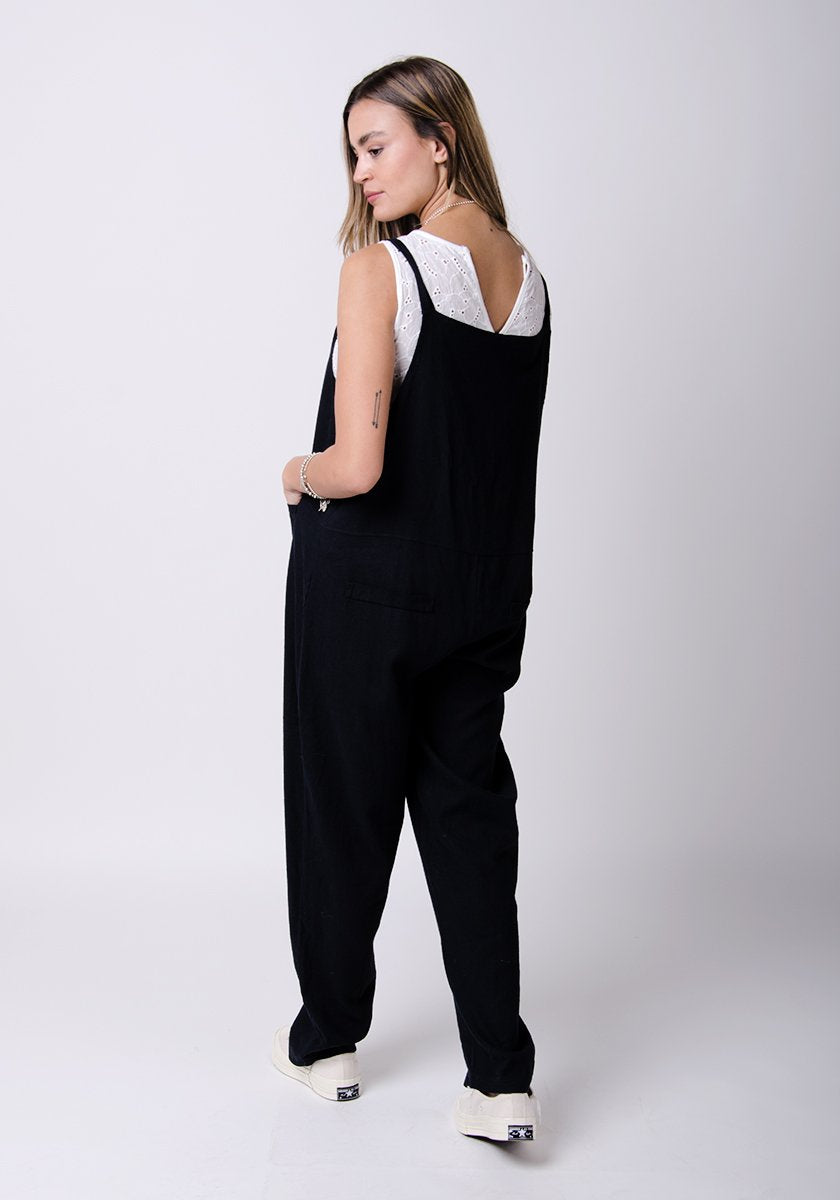 Full-rear pose looking to her left, showing adjustable straps and back pockets.