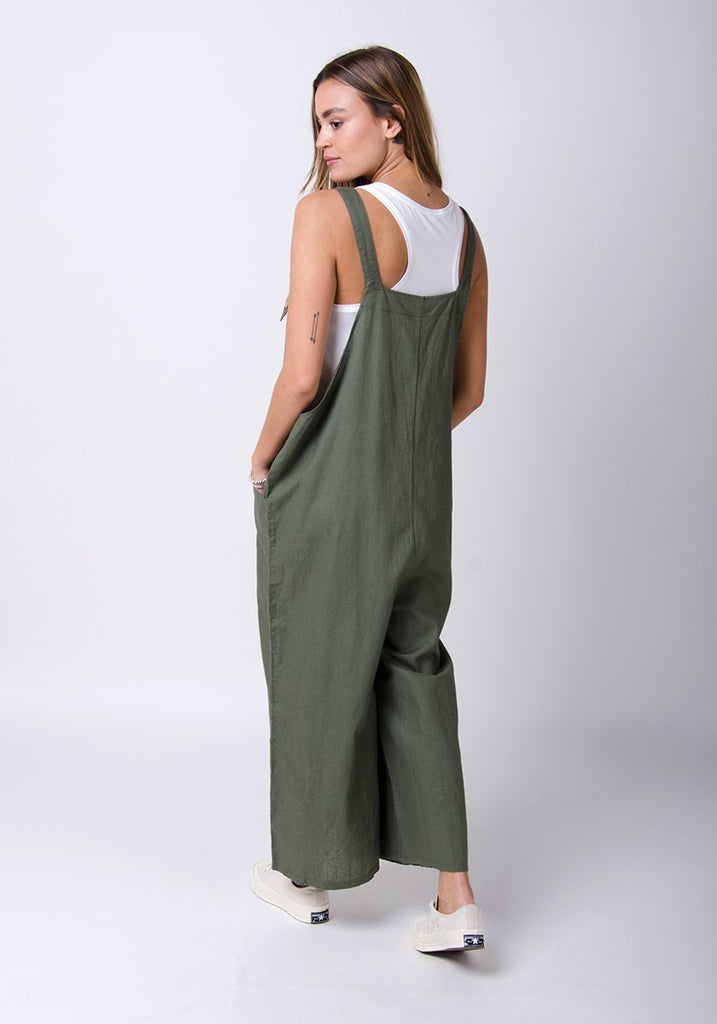 Full twisted back pose showing adjustable straps of green, wide leg overalls.