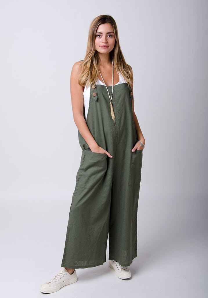 Full-length front pose with hands in front pockets wearing green Saffy-style, loose fit dungarees.
