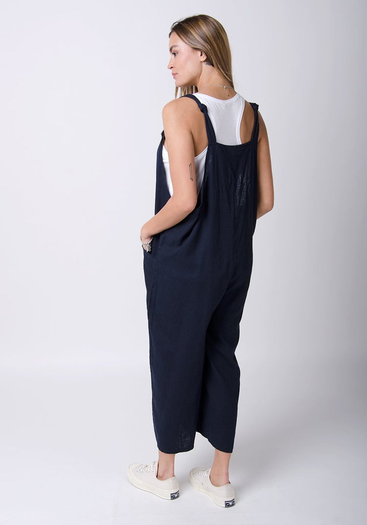 Full twisted back pose showing adjustable straps of navy-blue, wide leg overalls.