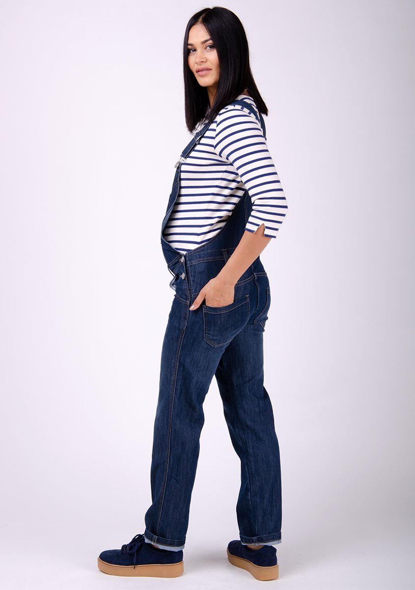 Full side pose to her right showing off bump wearing Dungarees Online’s dark wash blue denim dungarees.