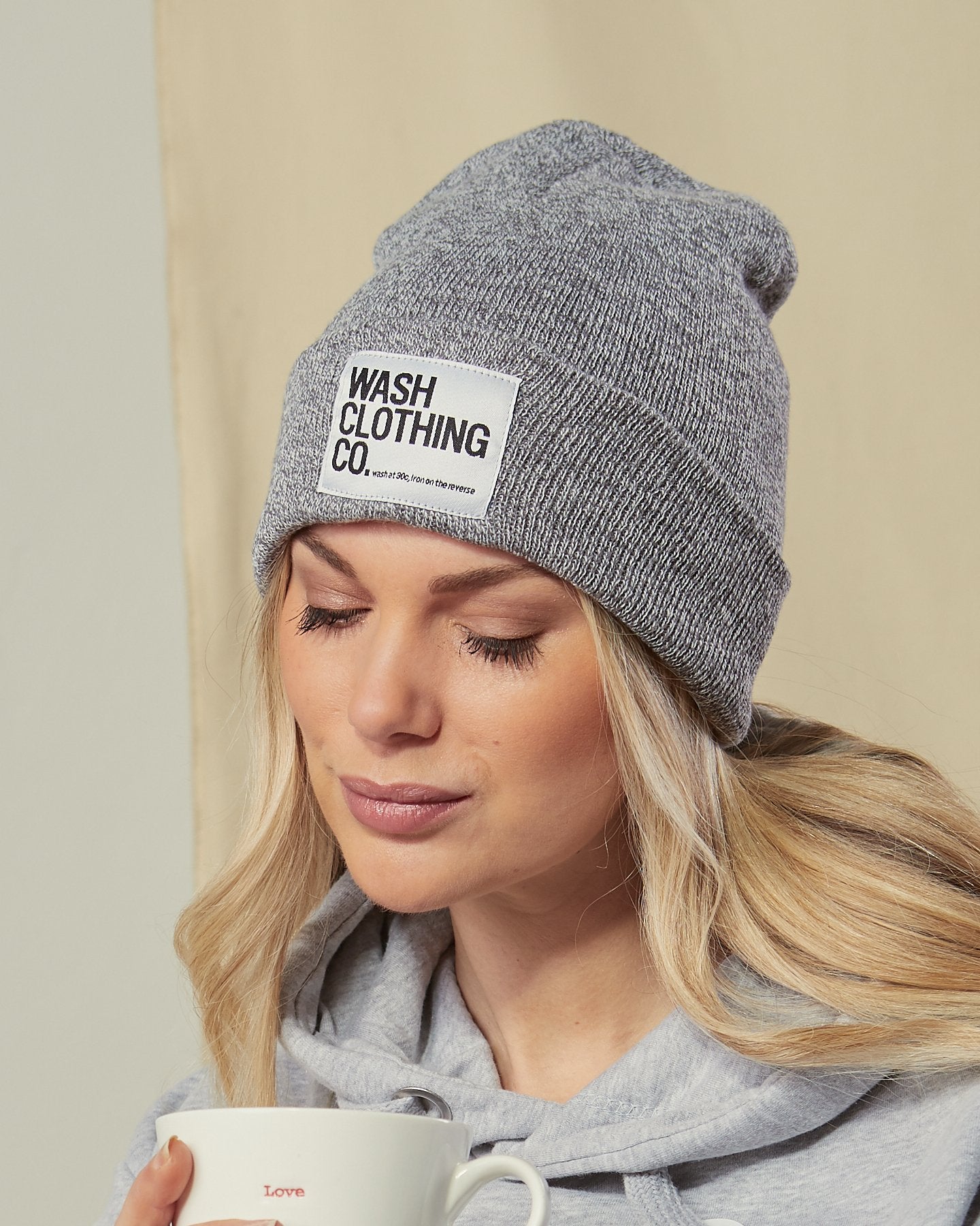Close-up of model looking down wearing Sinead grey cuffed beanie with view of WASH CLOTHING CO. label.
