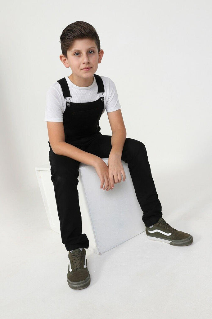 Side-view of boy sitting on box wearing durable, zip fly, machine washable dungarees in black cotton.