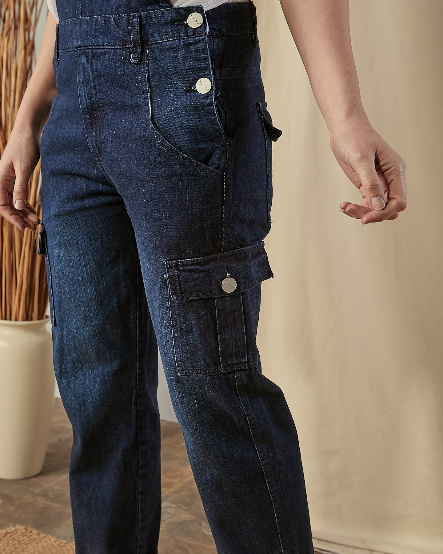 Close view of the leg of Tammy dark denim dungarees, clearly showing cargo pocket, side button fastening and denim texture.