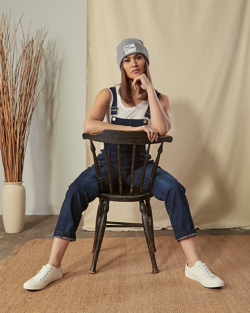 Front view sitting on a chair wearing Tammy dark blue denim regular fit dungarees.