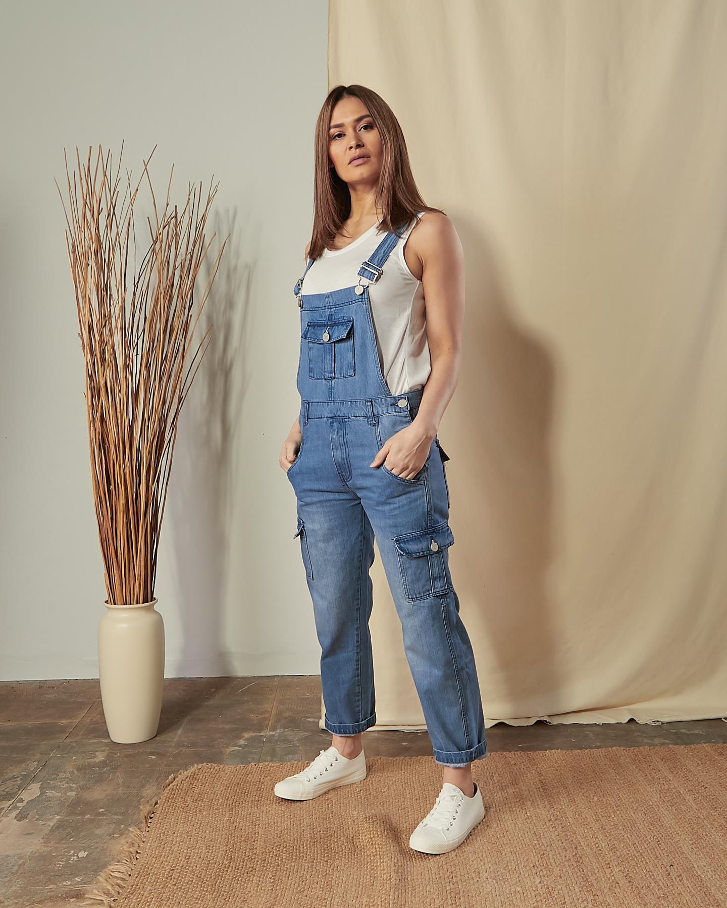 Full-length, angled front view of model wearing Tammy stonewash dungarees with hands in front pockets.