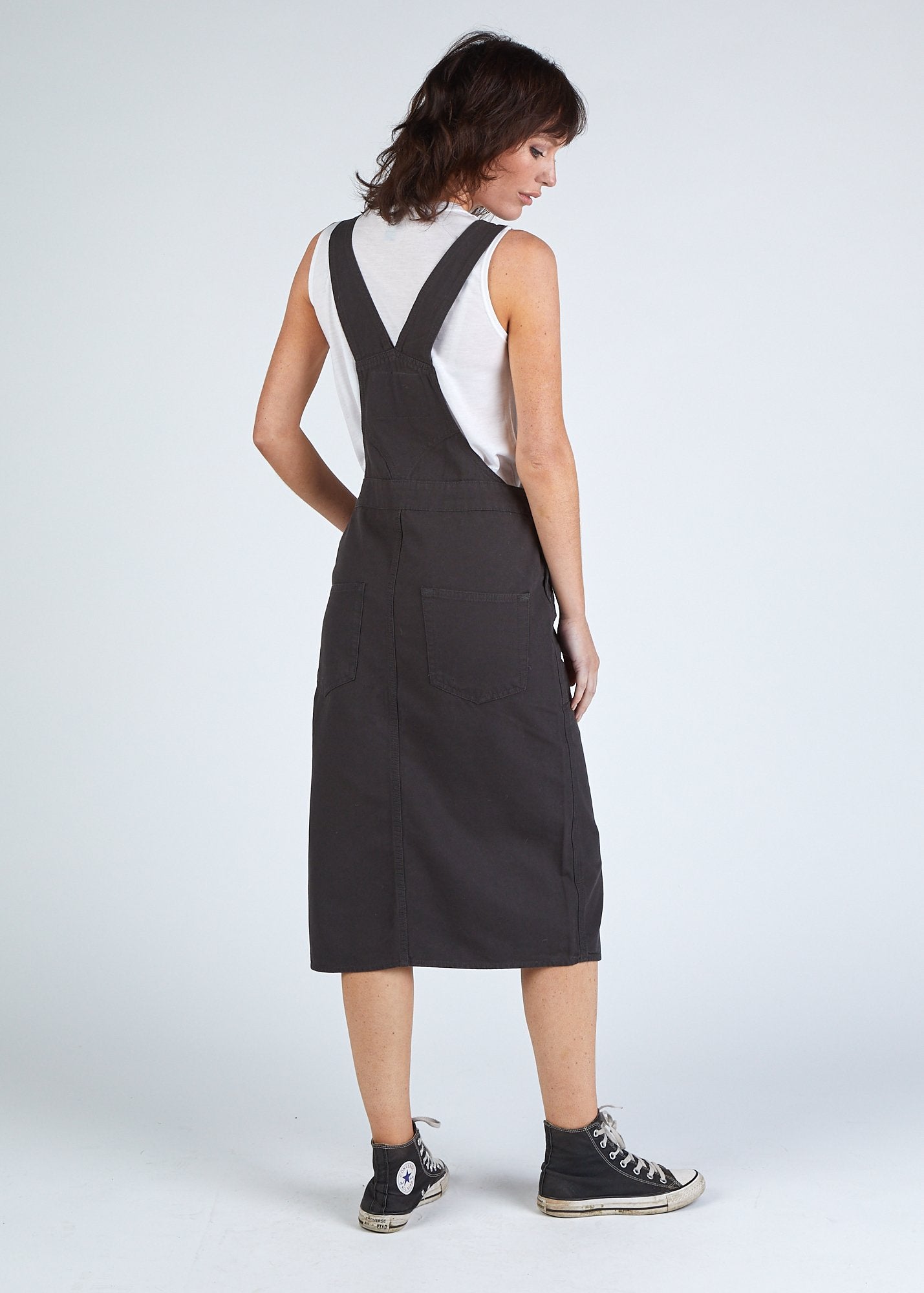Back shot faded black organic cotton bib-overall midi dress with view of back pockets and straps.