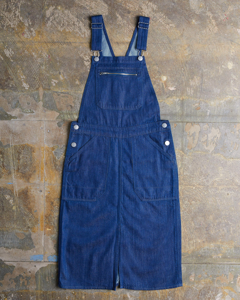 Full-length front flat shot of Uskees organic dark blue rinsed denim midi pinafore with showing pockets, zip bib-pocket and adjustable straps.