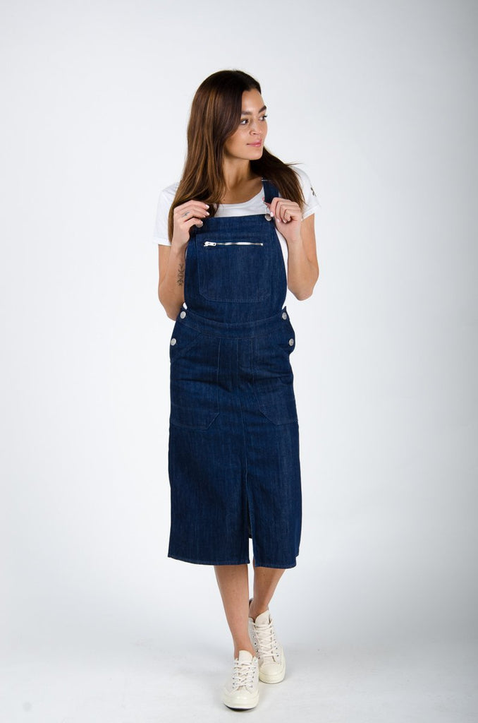 Front shot of dark blue rinsed Uskees organic cotton bib-overall midi dress with view of front split and deep front pockets.
