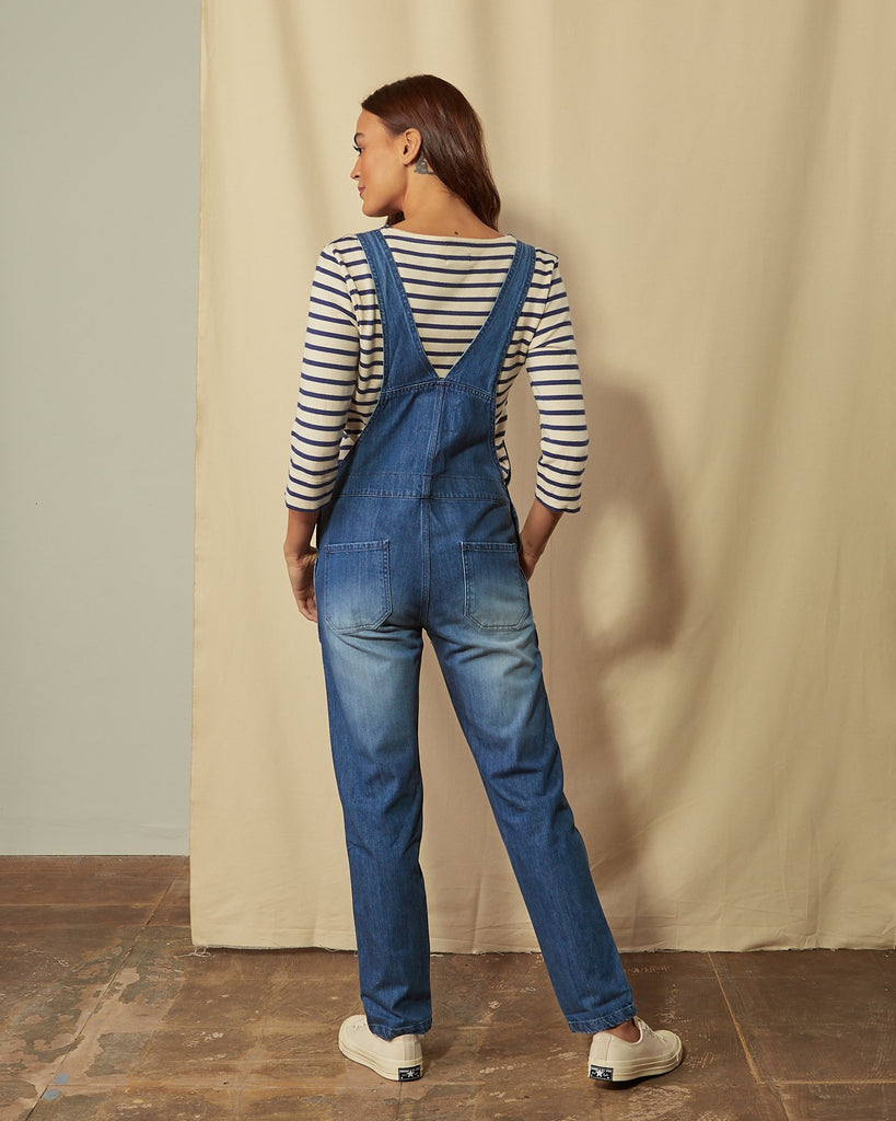 Back shot of women's washed organic denim bib-overalls with view of back pockets.